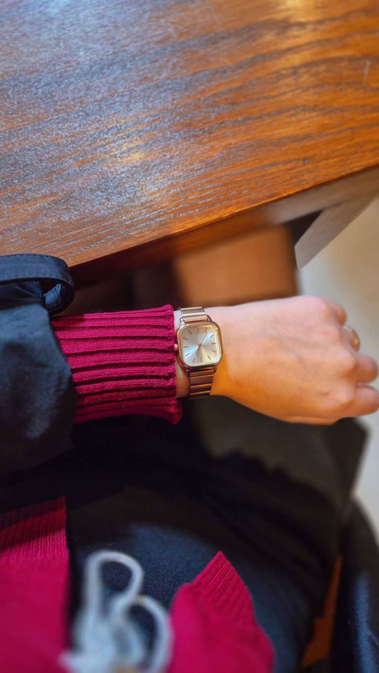 Close-up of a stylish wristwatch worn on a person's wrist indoors with wooden table background.