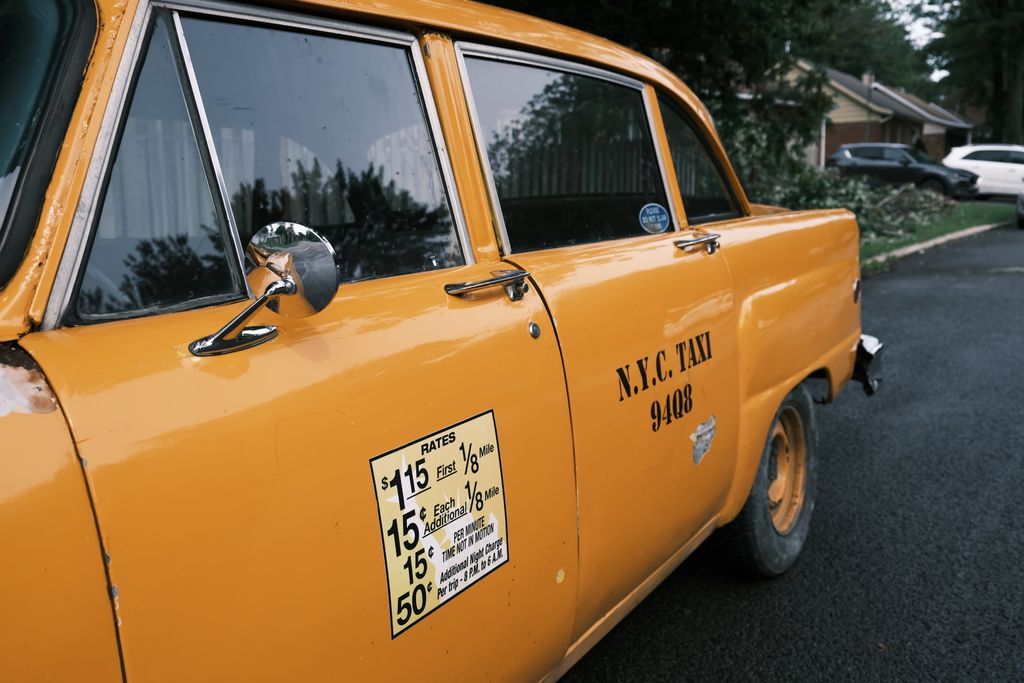 Close-up of a vintage yellow NYC taxi with iconic black lettering parked on a city street.